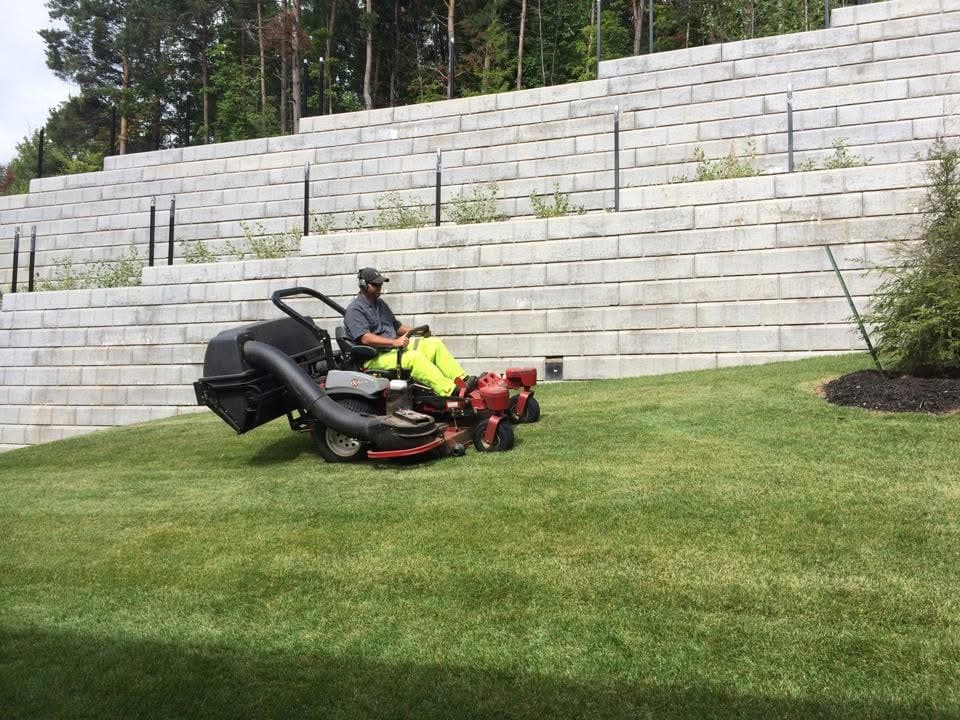Crew member mowing in front of massive multi-tiered retaining wall