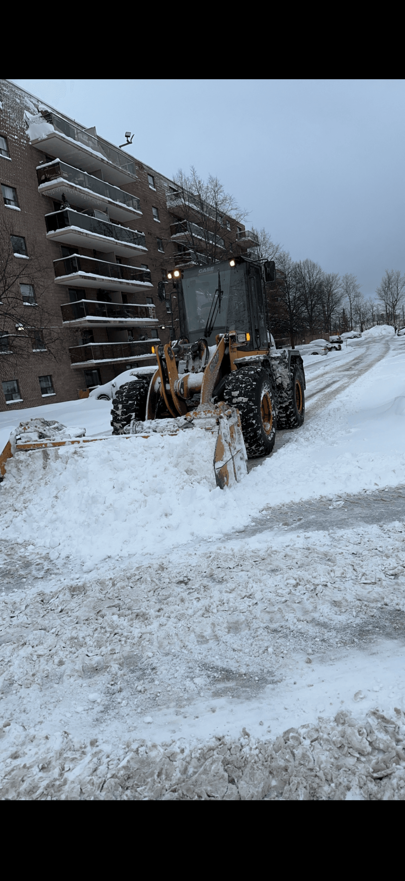 Large front-end loader clearing snow at apartment building